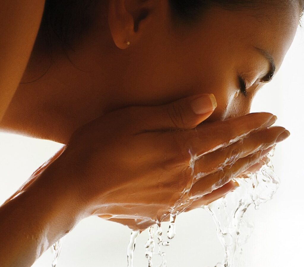 Close-up of a woman washing her face with water cupped in her hands.