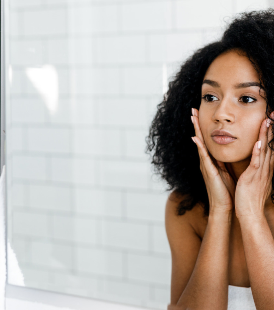 Woman looking into a mirror while gently touching both sides of her face.