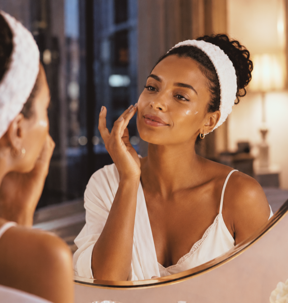 Woman applying cream beneath her eye while looking into a mirror.